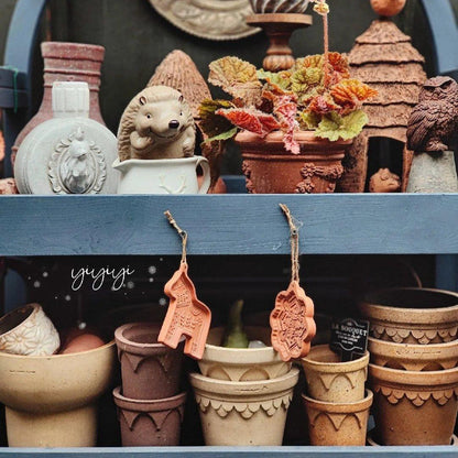 Assorted rustic earthenware planters with scalloped designs, arranged on a blue shelf with decorative pots, figurines, and hanging clay ornaments.