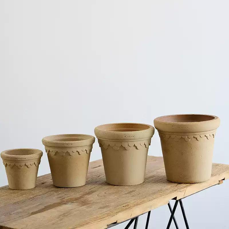 Set of ivory ceramic planters with scalloped edges in various sizes, displayed on a rustic wooden table.