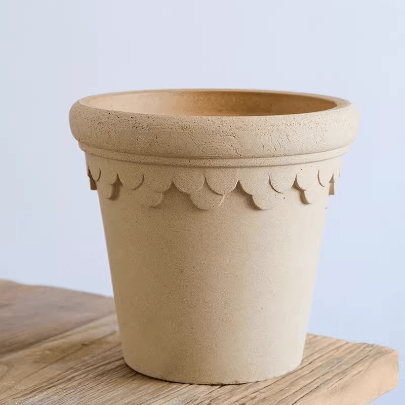 Ivory earthen flower container with scalloped trim, showcasing a simple, rustic design, positioned on a natural wooden surface.