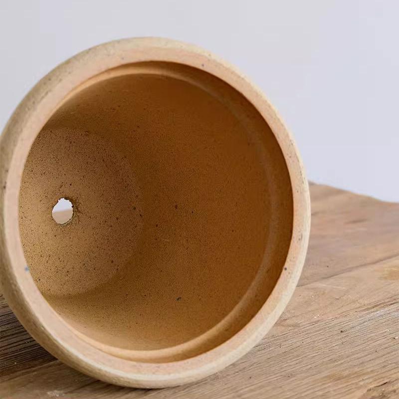 Clay planter with a drainage hole, showcasing a natural unglazed interior, placed on a wooden surface for optimal plant care.